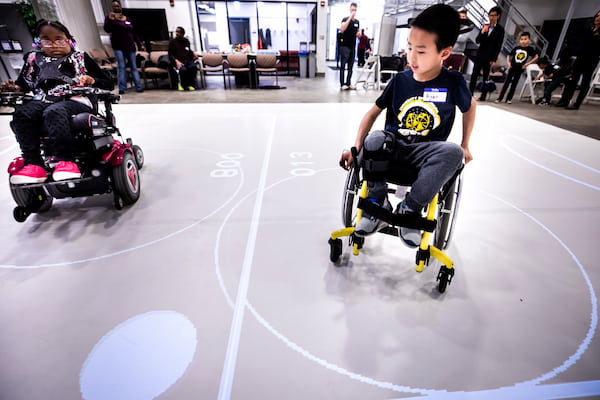 a boy in a manual wheelchair and a girl in a motorized wheelchair steer toward a projected "ball" on the floor of an augmented reality-assisted playspace